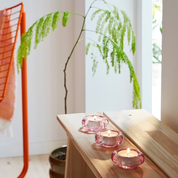 Three pink flower-shaped tealight holders on shelf near plant.