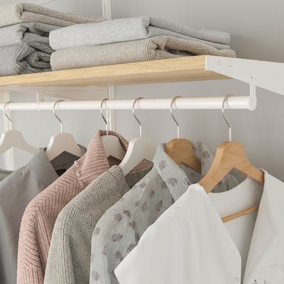 Folded blankets on top shelf, wooden hangers holding sweaters below. Organised closet storage.