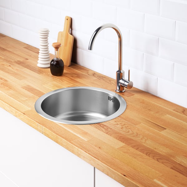 Stainless steel sink with wood countertop and chrome tap. Includes water trap and strainer. Efficient and durable design.