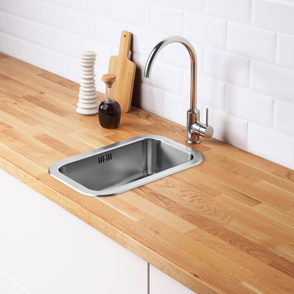 Stainless steel sink with modern tap on wooden countertop, including water trap and strainer.