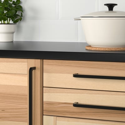 Modern kitchen drawers with light wood, black handles, and a plant.
