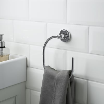 Chrished metal towel ring holds grey towel, mounted on tiled wall near sink.