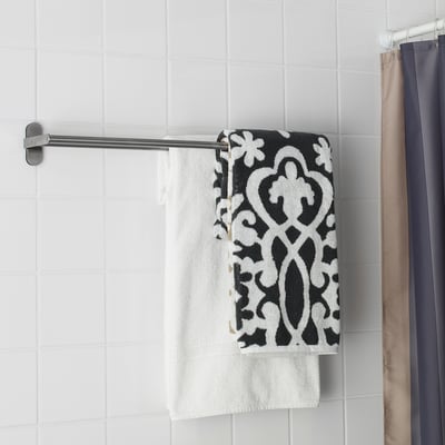A modern silver towel rack holds two towels: a patterned black and white one on top of a plain white one, mounted on a white tiled wall.
