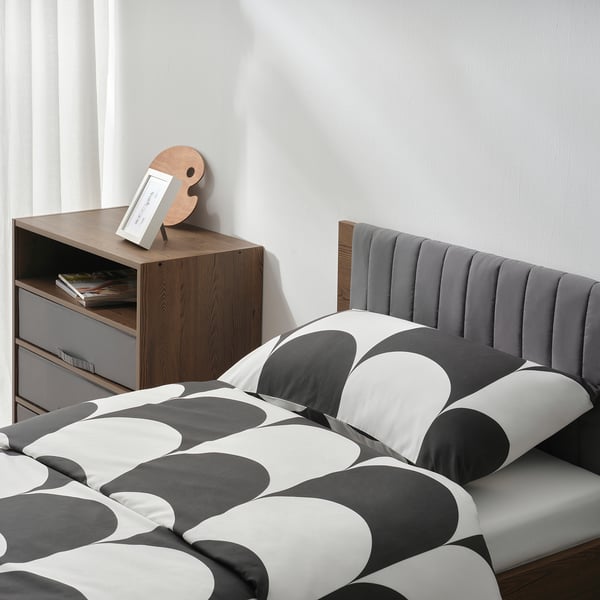 Modern bedroom with wooden bed, geometric bedspread, and bedside table with storage.