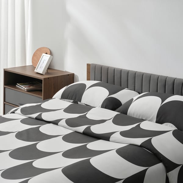 Bed with stylish, geometric-patterned comforter, wooden bedside table holding books and a picture frame.