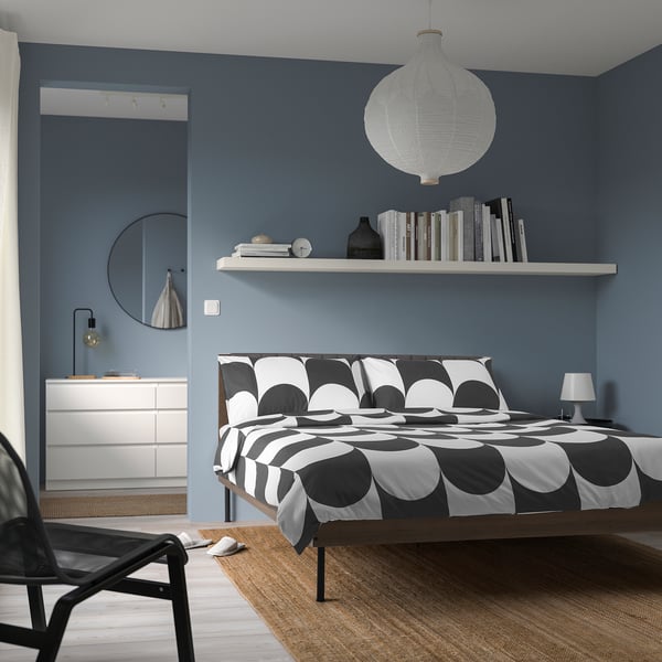 Bedroom with BRUKSVARA bed, white & black geometric print, wooden frame, tall by wall bookshelf.