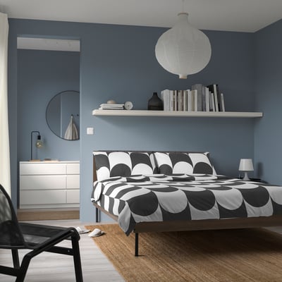 Bedroom with BRUKSVARA bed, white & black geometric print, wooden frame, tall by wall bookshelf.