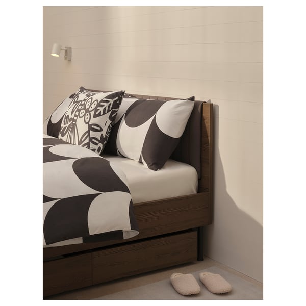 Bed with abstract pillows, soft headboard, brown colour, wood-like frame, cosy design.