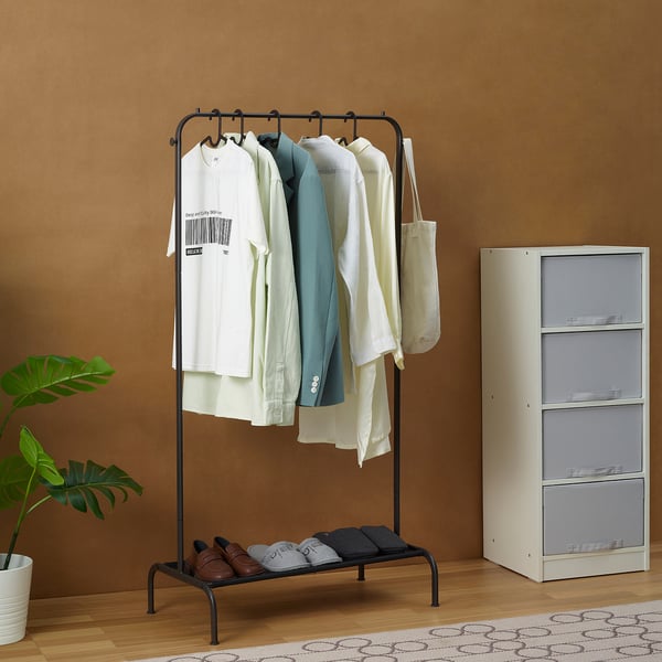 BRUKSVARA clothes rack in black with clothes and bag, next to large cabinet, with plant nearby.
