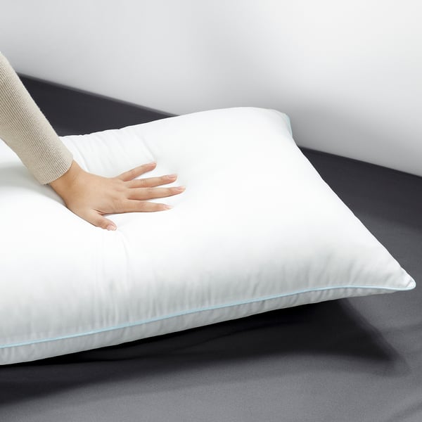 Hand touches soft, airy pillow on bed.