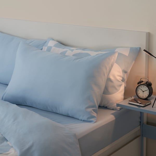 Bed with blue pillows and clock on bedside table.