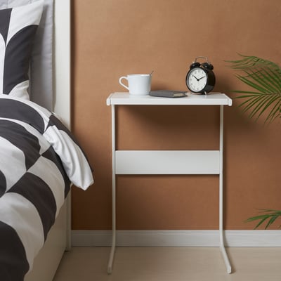 Bedside table with alarm clock, mug, and phone.