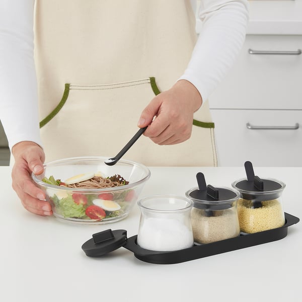 Person seasoning salad with different types of salt from a transparent glass container set, ensuring easy identification and no odours absorbed.