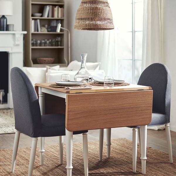 DANDERYD drop-leaf table, natural wood and white, compact with extendable leaves, sat between two grey chairs by a large window.