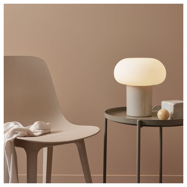 Minimalist interior with DEJSA lamp, beige, glass shade, chrome base, on round metal table beside beige chair.