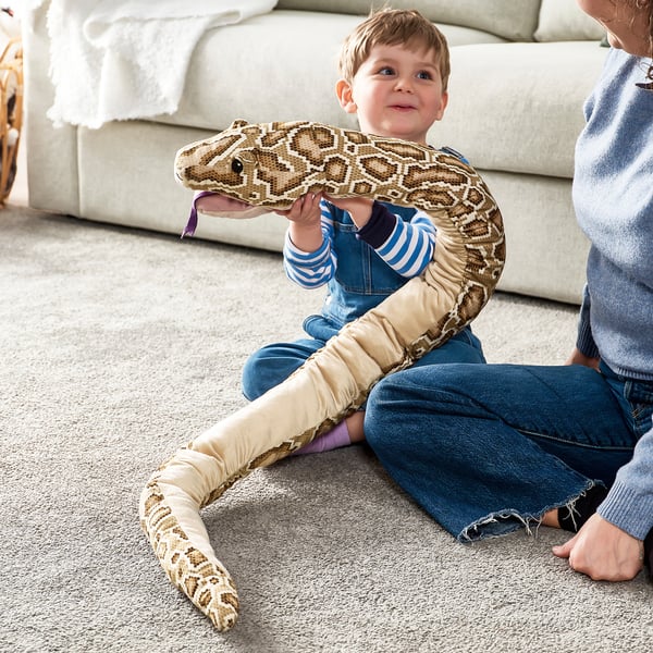 Boy plays with plush snake on carpet.