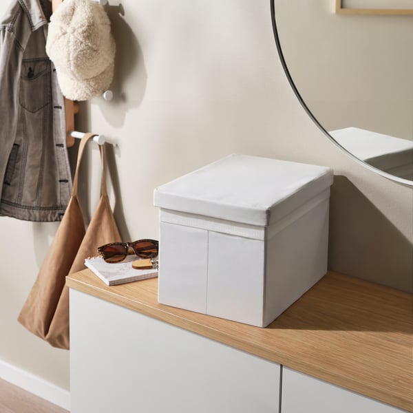 A white fabric box with lid on a wooden shelf, holding sunglasses and a book. The box has integrated handles for easy access.