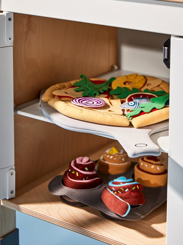 A wooden play kitchen set with fake pizza and baked goods in bright colours.