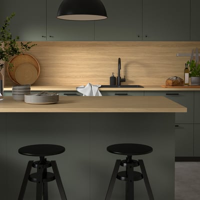 Modern kitchen island with EKBACKEN light wood countertop, black bar stools and green cabinets, featuring a sleek, clean design.