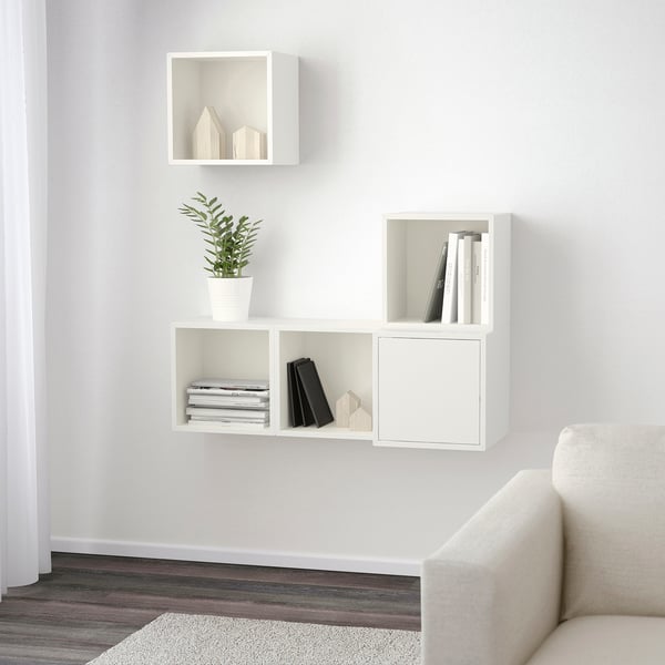 White wall-mounted shelves holding books, plants, and decorative items, part of the EKET storage system.