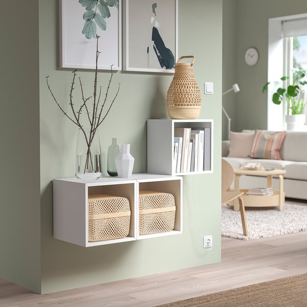 Minimalist living room with light green walls, white EKET shelves, baskets, and vases, natural light.