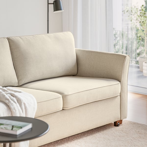 Beige sofa-bed with wooden legs; transforms into a bed, near a coffee table with a magazine.