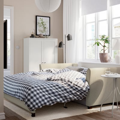 Modern living room with grey/white sofa-bed, stylish legs, under tall windows.