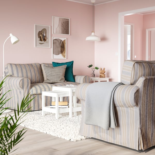 Modern living room: striped beige sofa, teal pillows, white coffee table, pink walls, minimalist art, cosy lamps, houseplant.