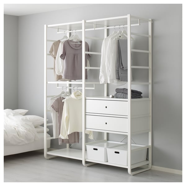 Modern ELVARLI wardrobe with open shelves, hanging rods, and drawers, displaying neatly organised clothes beside a bed.