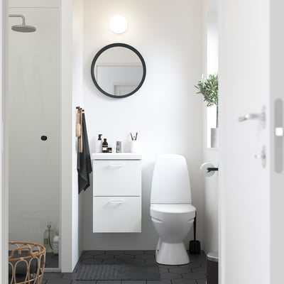 Modern minimalist bathroom with white ENHET vanity, round mirror, toilet, shower, and dark hexagon floor tiles.