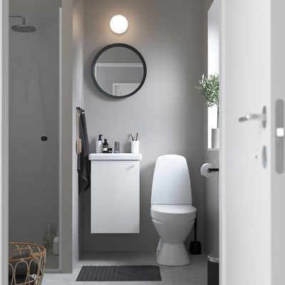 Modern grey bathroom with white ENHET cabinet, round mirror, and toilet. Sleek design, efficient space use.