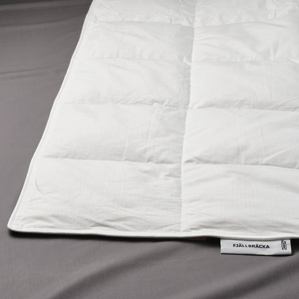 A neatly spread white duvet with box-stitch pattern indicating high quality, shown on a grey bedding. The tag “FJÄLLBRÄCKA” is visible.