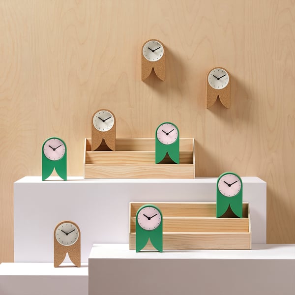 Aerial view of green & cork FLODKRÄFTA clocks on white walls with wooden background.