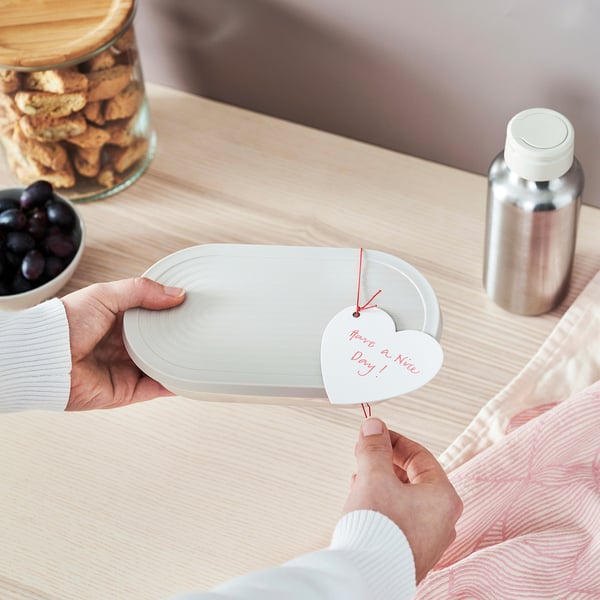 A person holds a heart-shaped tag reading have a nice day attached to a round placemat, demonstrating reusable labelling for gifts or food containers.