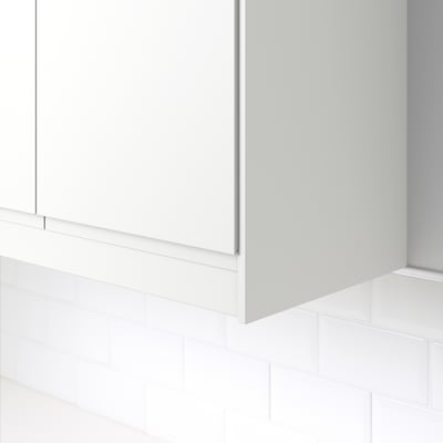 White kitchen cabinet trim, hiding cables, mounted on tiled wall.