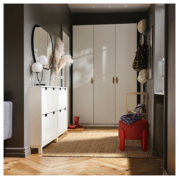 Modern entryway with white storage units, a round mirror, dried flowers, a red stool, bags, boots, and a rug.