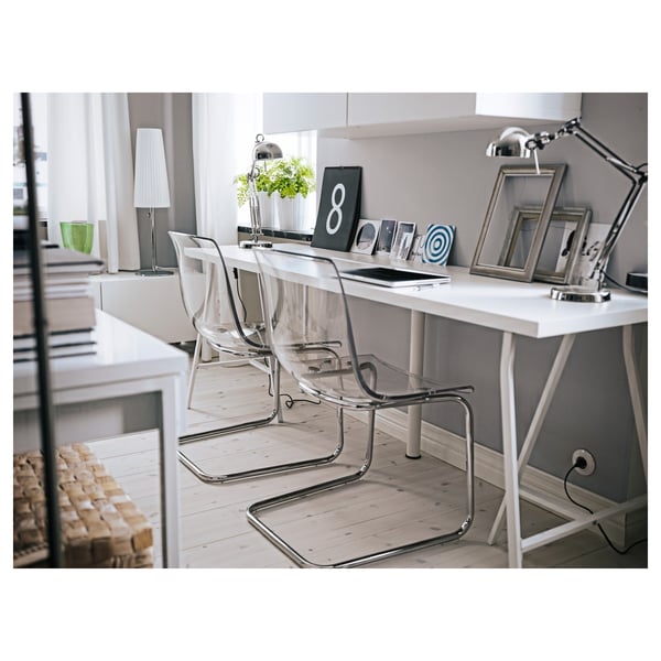 Modern office desk with clear chairs, white lamp, and decorative items.