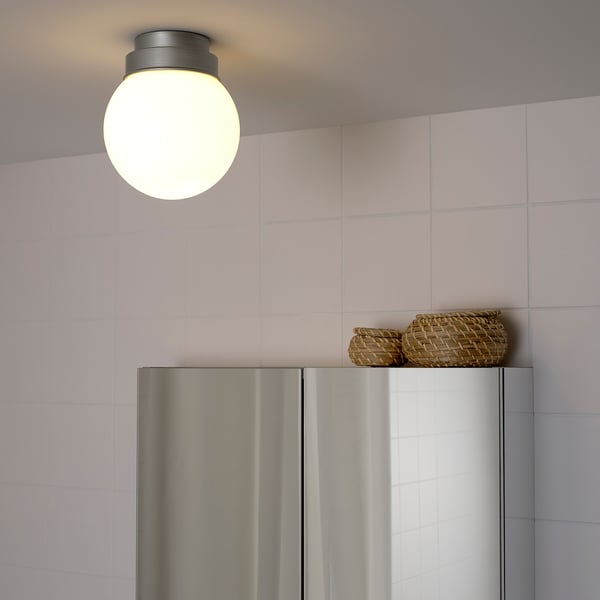 A round ceiling light with a glass shade emits soft light over a stainless steel refrigerator, two woven baskets on top.