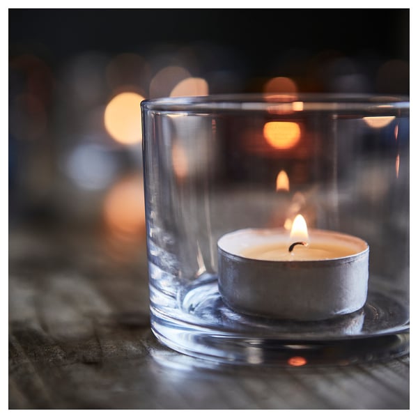 Glass candle holder encases a lit tea light, casting soft, warm light. Elegant design enhances cosy ambiance.