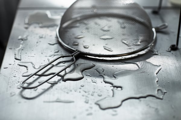 Black and white a round metal strainer with towel underneath on a wet countertop.