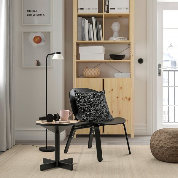 Scandinavian-style side table GRIMSARBO, black with wooden top and metal base, near chair, compact.