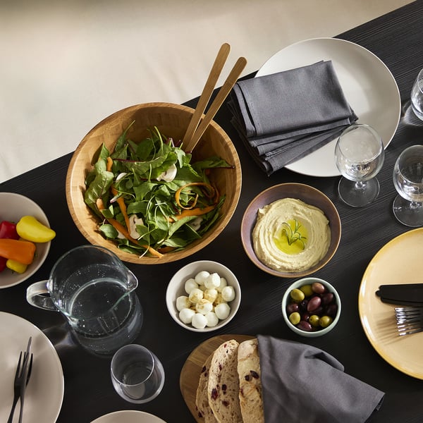 Large wooden salad bowl with greens, central on dining table.