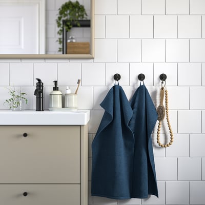 Modern bathroom: blue towel on black hooks beside white tiles.