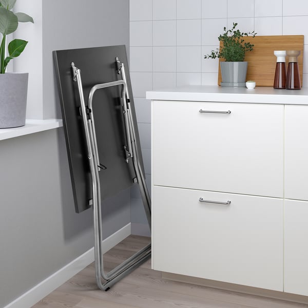 Foldable kitchen table leans against cabinet, ready for use.