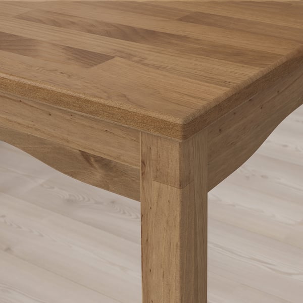 Close-up of a wooden tables edge, showcasing its polished, light brown surface and sturdy wooden leg with visible grain patterns.