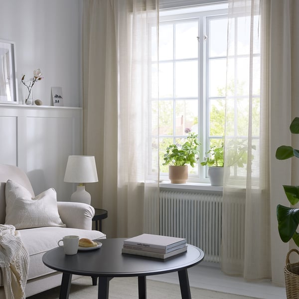 Modern living room with sheer curtains, sofa, coffee table & plants.