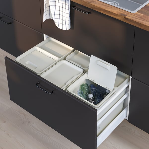 Black kitchen drawer with three white waste sorting bins, each with lids, organised under a wooden countertop.