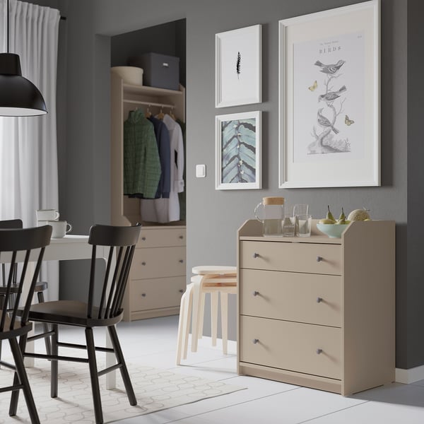 Modern living space with HAUGA light beige chest, art prints, wooden chairs, and open closet.