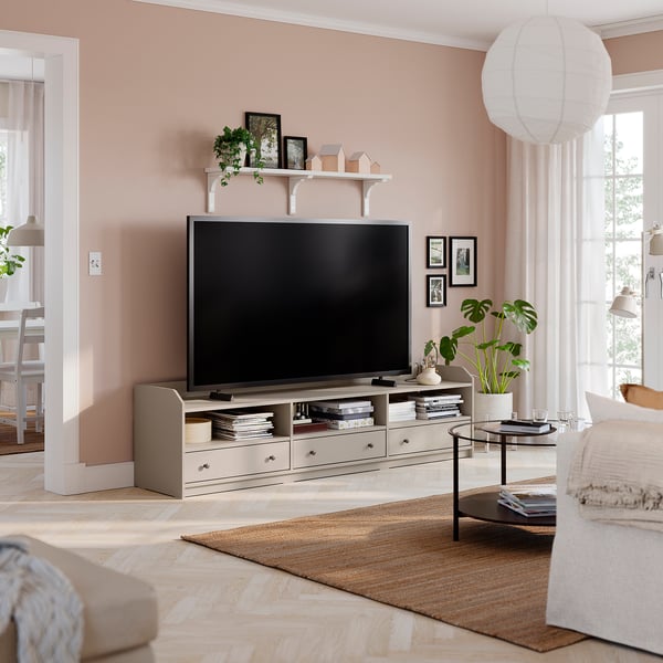 Modern living room with HAUGA tv unit, flat-screen tv, decorative shelf, pink walls, beige sofa, wooden floor, coffee table, rug, and pendant light.