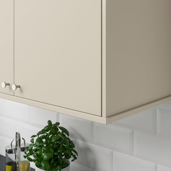 Beige kitchen cabinet with circular knobs, hiding lighting units. A green plant and oil dispenser sit on the counter.